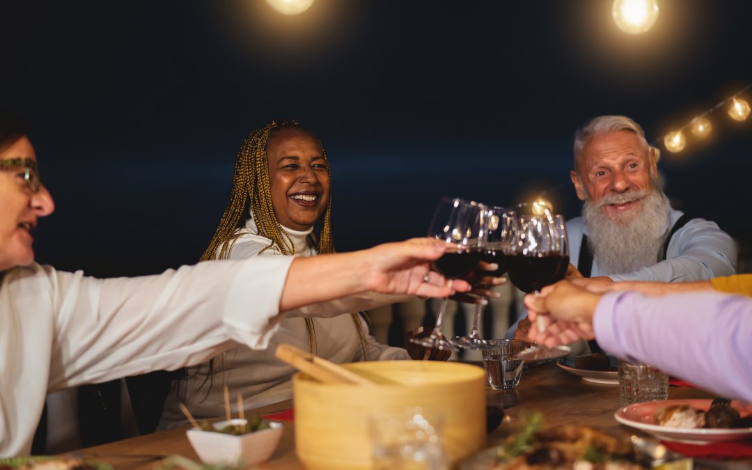 Happy multiracial senior friends toasting with red wine glasses together on house patio dinner